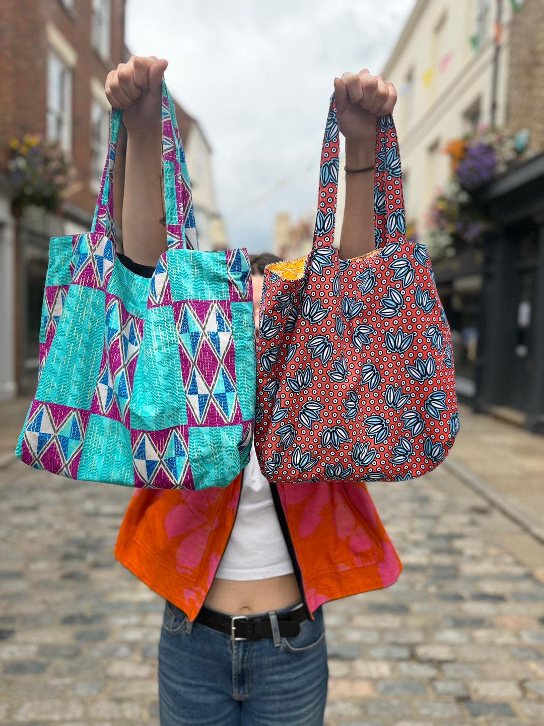 Two handmade lined tote bags in colourful print fabrics held up on Burgate, Canterbury